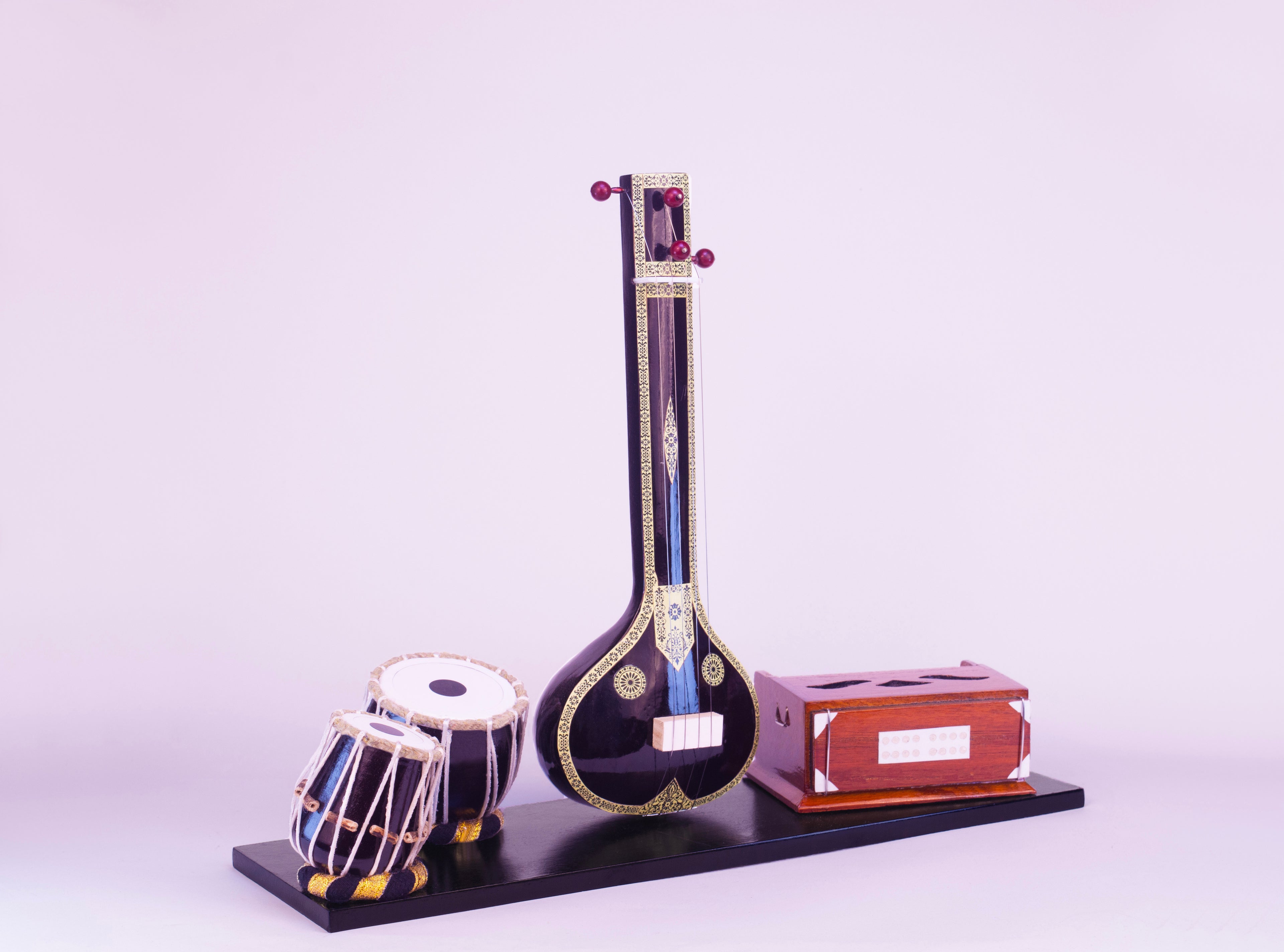 Model of a sitar, tabla, and other instruments on a stand with a light purple background